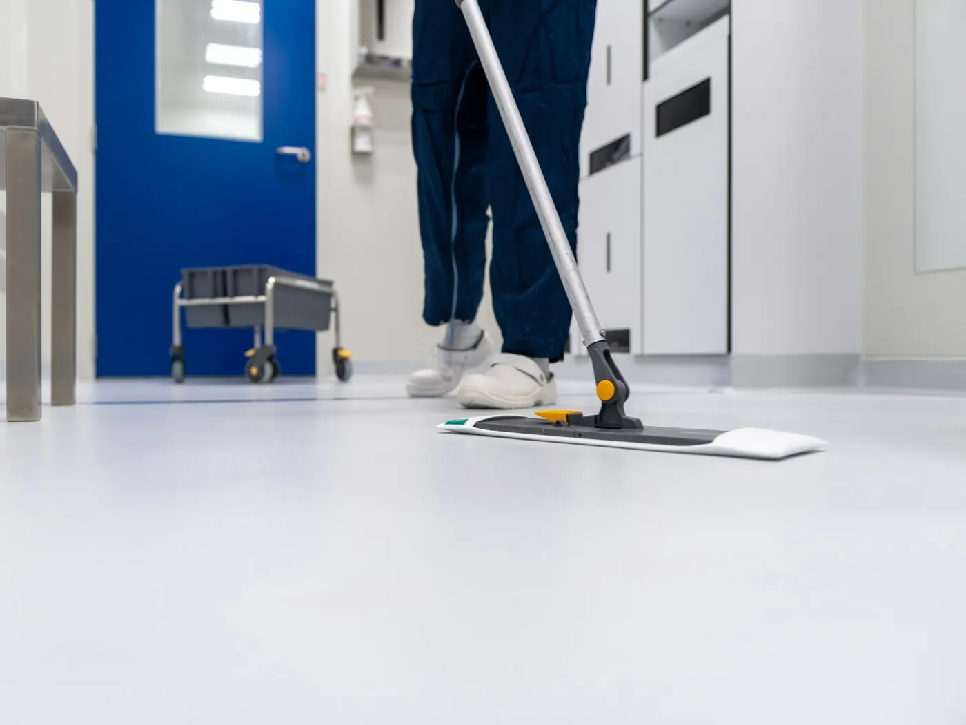 A cleaner mopping a smooth, light-coloured floor with a flat mop